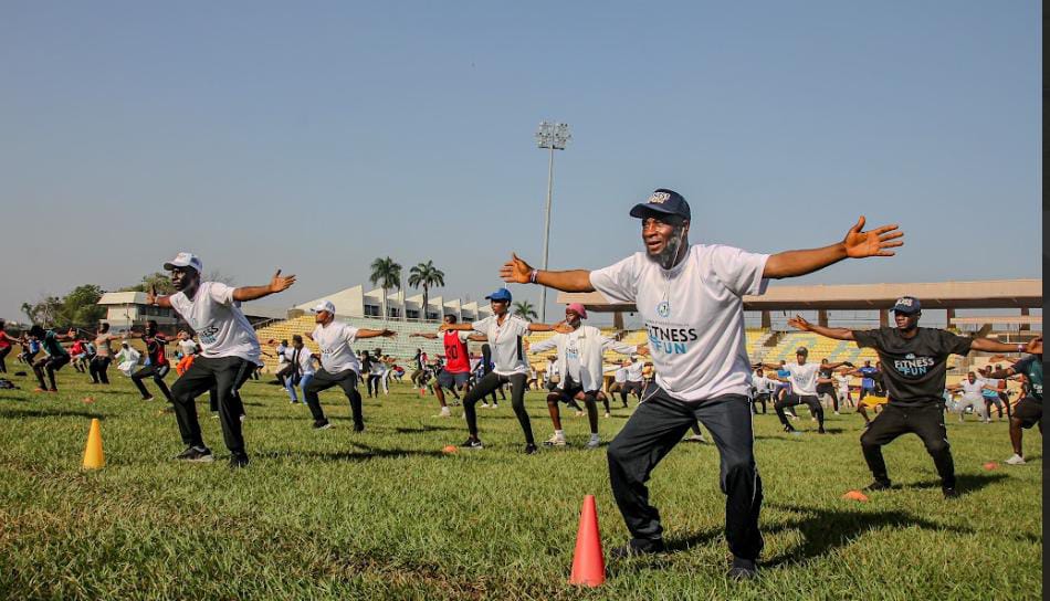 Coach Korede leading a large outdoor aerobics session at a stadium